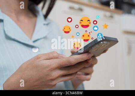 Nahaufnahme von Frauenhänden, die ein Smartphone halten, mit bunten Emoji-Reaktionen in sozialen Medien, die über ihnen schweben, Kommunikationskonzept, Online-Interaktion, di Stockfoto