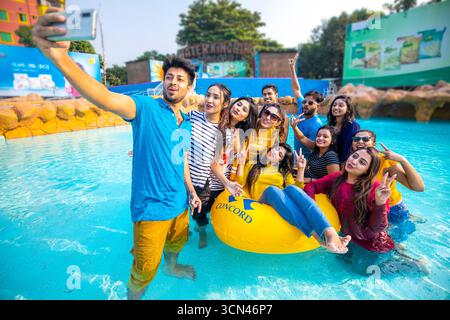 Eine vielfältige Gruppe von Freunden, die an einem sonnigen Tag in einem Wasserpark ein lustiges Selfie in einem Swimmingpool machen. Stockfoto