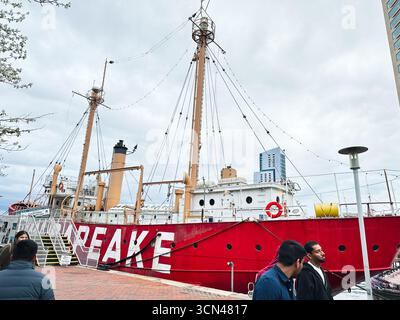 Baltimore, Maryland, USA - 10. April 2025: Ein leuchtend rotes US-Leuchtschiff Chesapeake, das in Baltimore, USA, mit Touristen und urbanem Himmel vor Anker liegt Stockfoto