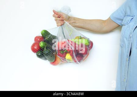 Frau, die frisches Obst und Gemüse in umweltfreundlichen wiederverwendbaren Beuteln in ausgestreckter Hand auf weißem Hintergrund hält. Umweltfreundliches Wohnen und keine Verschwendung beim Einkaufen Stockfoto