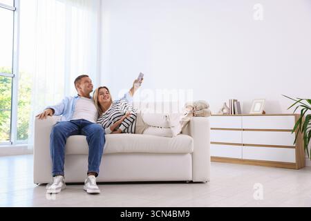 Frau und Mann, die die Klimaanlage auf dem Sofa zu Hause per Fernbedienung steuern Stockfoto