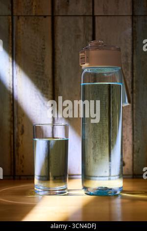 Ein filmisches Stillleben mit einem Glas und einer Flasche Süßwasser, mit einem dramatischen Sonnenstrahl, der eine friedliche und achtsame Atmosphäre schafft. Ein Konzept für Hydraten Stockfoto