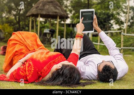 Ein entspanntes Paar liegt draußen auf dem grünen Gras, eine Frau in einem orangefarbenen Saree und ein Mann in einem hellen Hemd. Stockfoto