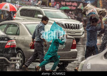 Heftiger Monsun-Regen auf der geschäftigen Stadtstraße | offenes Foto von Menschen, die in der asiatischen Stadt Dhaka nach Unterschlupf stürmen | urbanes Chaos im Regenguss Stockfoto
