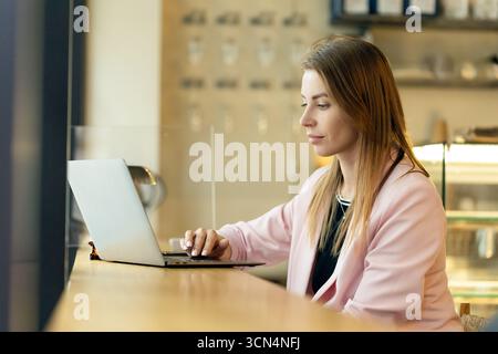 Junge Frau Porträt, die mit Laptop im modernen Stadtkaffee arbeitet Stockfoto