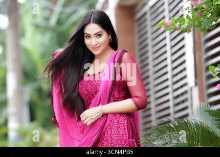 Eine wunderschöne südasiatische Frau mit langen Haaren lächelt sanft, während sie ein traditionelles rosafarbenes Outfit mit einer passenden Dupatta im Freien trägt Stockfoto
