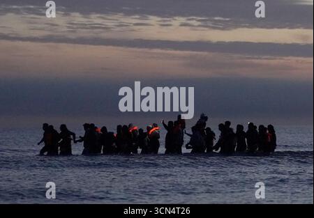 Eine Gruppe von Menschen, die als Migranten gelten, waten ins Meer, um ein kleines Boot in Gravelines, Frankreich, zu treffen. Bilddatum: Freitag, 19. September 2025. Stockfoto