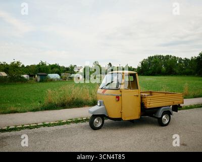 Gelber dreirädriger Affen, der auf einer Landstraße geparkt ist Stockfoto