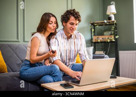 Erwachsenes Paar, das im Wohnzimmer auf dem Bett sitzt und einen Online-Arzttermin mit Laptop hat. Stockfoto