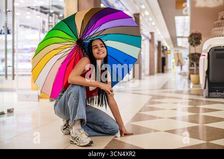 Mädchen mit Zöpfen hält Regenbogenschirm im Einkaufszentrum. Stockfoto
