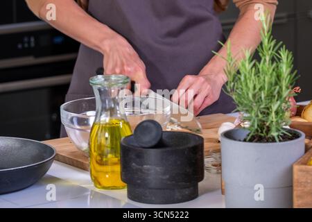 In einer modernen Küche zerkleinert die Chefköchin frisches Gemüse mit Kräutern und Kochzutaten in der Nähe, um eine lebendige kulinarische Zubereitung zu kreieren Stockfoto