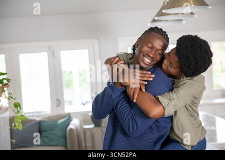 afroamerikanisches Paar umarmt sich neben der Kücheninsel unter Hängeleuchten zu Hause Stockfoto