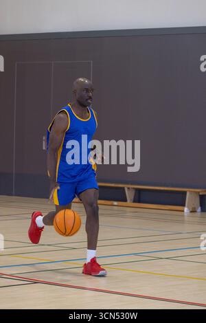 afroamerikanischer Mann in blau-gelber Uniform, der Basketball über den Fitnessraum dribbelt Stockfoto