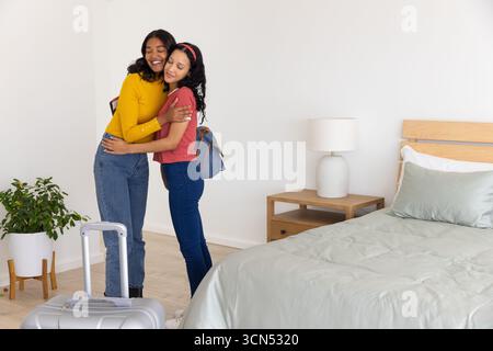 Verschiedene Eltern und Teenager-Tochter umarmen sich in der Nähe des Koffers im beleuchteten Schlafzimmer, Kopierraum Stockfoto