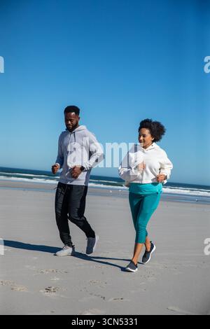 Verschiedene Freunde, die entlang der Sandküste laufen, tragen Laufschuhe, Smartwatch und Fitness-Tracker Stockfoto