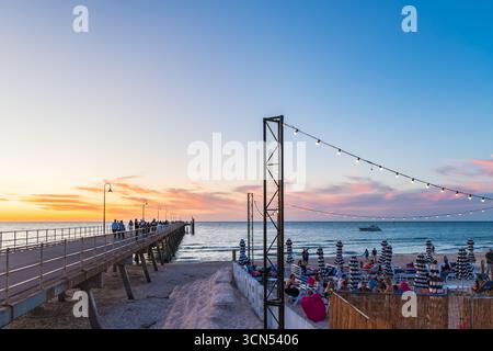 Adelaide, Südaustralien – 22. Dezember 2023: Menschen wandern auf dem Glenelg Jetty mit dem Moseley Beach Club und genießen den Sonnenuntergang in einem heißen Sommer Stockfoto