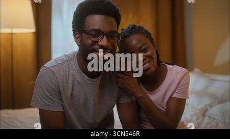 Glückliche Liebe, die afroamerikanische Familie zu empfangen, verheiratet, fröhliches Paar Porträt Ehepartner Mann Mann und Frau Frau, die sich umarmen, kuscheln, sitzendes Bett und Blick auf das Bett Stockfoto