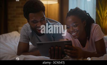 Interessierte lachen glückliche afroamerikanische Familie ethnisch verheiratete Ehepaar Ehemann mit digitalen Tablet Online-Inhalten lustige Komödie Stand-up Stockfoto