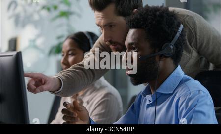 Multiethnische Teamarbeit im Callcenter-Büro kaukasischer männlicher Vorgesetzter gibt Anweisungen afrikanischer Callcenter-Betreiber Headset nickt Kopf indische Frau Stockfoto