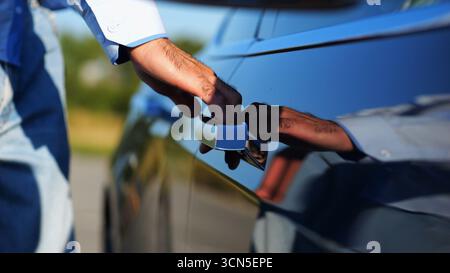 Nah an der männlichen Hand eines Geschäftsmannes, der die Tür öffnet und in ein modernes Elektroauto einsteigt. Der Arm des Unternehmers öffnet die Tür und setzt sich in den Stockfoto