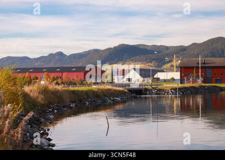 Orkanger Industrial Port View, Norwegen. Küstenlandschaft mit roten Holzscheunen und wolkenblauem Himmel Stockfoto