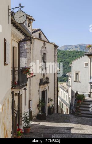Blick auf sonnendurchflutete Architektur, lebendige Blumen, die von Balkonen herabfallen, und Kopfsteinpflastertreppen, die in die Ferne führen, Rivisondoli, Abruzzen, Italien. Stockfoto