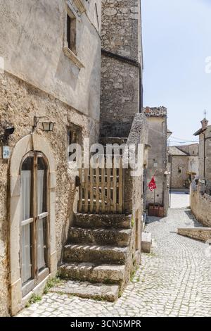 Blick auf rustikale Steintreppen, die zwischen alten Gebäuden hinaufsteigen, ein malerisches Holztor, das den Weg in Santo Stefano di Sessanio, Abruzzen, Italien, bewacht. Stockfoto
