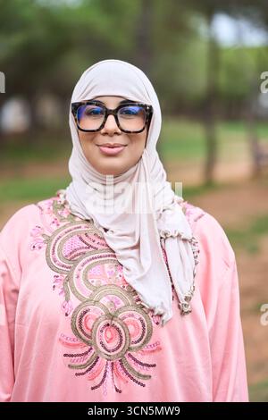 Muslimische Frau mit Hijab und Brille, die draußen lächelt Stockfoto