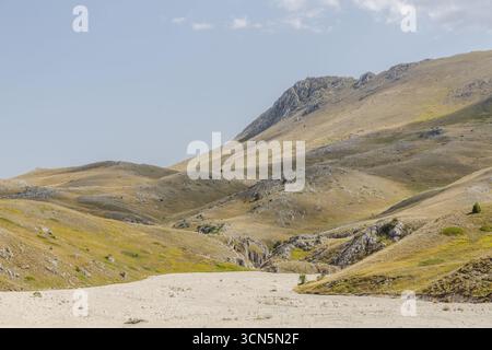 Blick auf sonnendurchflutete Täler und zerklüftetes Gelände, das sich zu einem Tableau natürlicher Schönheit unter einem ruhigen Himmel vereinigt, Isola del Gran Sasso D'italia, Abruzzen, Italien. Stockfoto