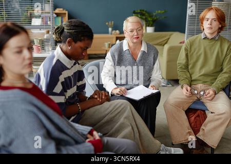 Weiße Frau mittleren Alters, die Gruppentherapie mit verschiedenen Menschen führt Stockfoto