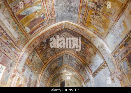 Blick auf lebendige Fresken an der gewölbten Decke einer historischen Kirche, in sanftem Licht getaucht, das durch alte Wände filtert, Bominaco, Abruzzen, Italien. Stockfoto