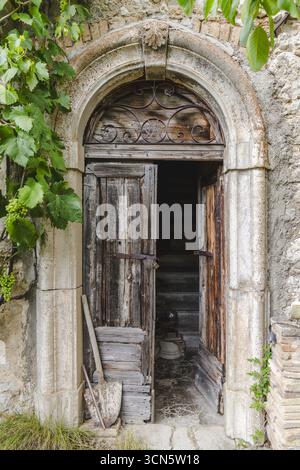 Blick auf eine alte Holztür, die einen Blick auf eine Treppe bietet, die von einem Steinbogen mit Vegetation eingerahmt ist, in Frattura Vecchia, Abruzzen, Italien. Stockfoto