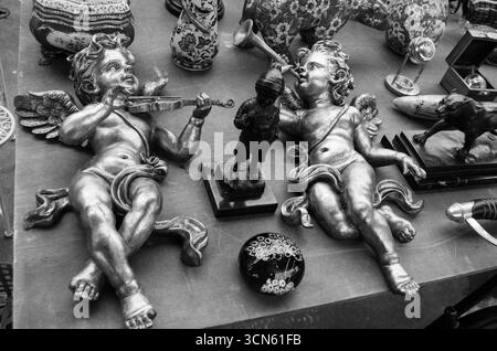 Flohmarkt in Paris, Frankreich. Zwei goldene Engel spielen Geige und Trompete. Stilleben-Postkarte im Retro-Stil. Schwarzweißes historisches Foto. Stockfoto