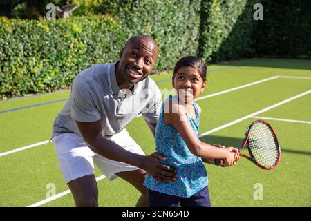 Verschiedene Vater und Tochter knieten beim Tennisschaukeln auf Kunstrasen und halten Schläger Stockfoto