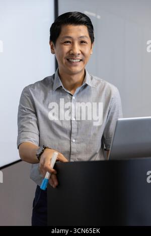 asiatischer Mann mittleren Alters, der hinter dem Podium im Konferenzraum steht, mit Markierungen und Laptop Stockfoto