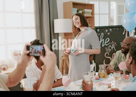 Kaukasische schwangere junge Frau lächelt, während sie Cupcakes bei der Babyparty hält Stockfoto