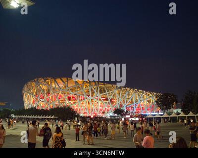 Das Pekinger Nationalstadion, bekannt als „Vogelnest“, beleuchtet bei Nacht, mit Menschen im Vordergrund und präsentiert eine moderne Architektur Stockfoto