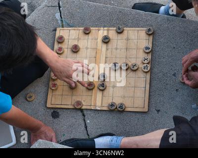 Ein Blick von oben auf eine Gruppe von Menschen, die chinesisches Schach (Xiangqi) auf einem Holzbrett auf der Straße spielen, was einen beliebten kulturellen Zeitvertreib hervorhebt. Stockfoto