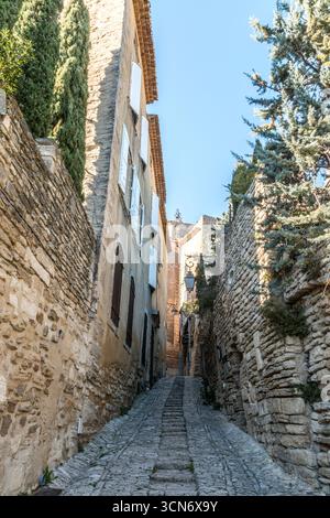 Frankreich - Gordes - Steinweg - steile Kopfsteinpflasterpassage zwischen hellen Wänden steigt in Richtung Licht, Fensterläden und Efeu und folgt einem ruhigen provenzalischen Aufstieg Stockfoto