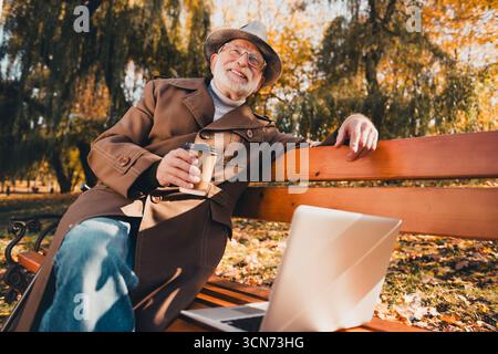 Senior Gentleman entspannt sich in einem Herbstpark und genießt die saisonale Landschaft und Freizeit an einem sonnigen Tag im Freien Stockfoto