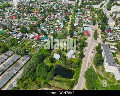 Ein Blick aus der Vogelperspektive auf Gus Chrustalny mit Wohnhäusern, einem kleinen Teich und einer einzigartigen Kapelle mit urbanen Blöcken im Hintergrund. Stockfoto