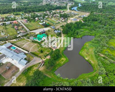 Eine große Luftaufnahme eines großen Herrenhauses mit einem hellen grünen Dach, einem kleinen Teich und einem Wohngebiet mit einem üppigen grünen Wald im Hintergrund. Stockfoto
