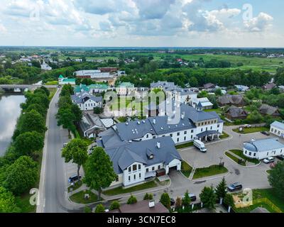 Ein Panoramablick auf Suzdal aus der Vogelperspektive mit einer Mischung aus modernen und historischen Gebäuden auf einer Straße neben einem Fluss mit einer Brücke, mit grünen Feldern im Stockfoto
