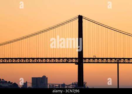 Brücke Ponte 25 de Abril Lissabon Portugal / LISSABON, Portugal — die Ponte 25 de Abril, eine markante rote Hängebrücke, überspannt den Tejo und verbindet Lissabon mit der Gemeinde Almada. Dieses berühmte Wahrzeichen, das oft mit San Franciscos Golden Gate Bridge verglichen wird, dient als wichtige Verkehrsader für Straßen- und Schienenverkehr. Die markante Silhouette ist ein integraler Bestandteil der Skyline von Lissabon, und die 1966 fertiggestellte Brücke ist eine der längsten Hängebrücken Europas. Stockfoto