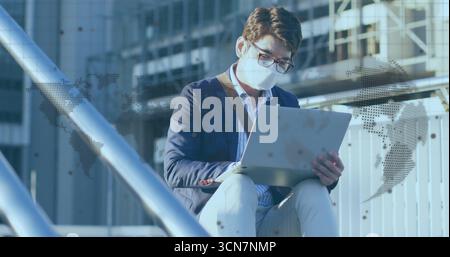 Arbeitender asiatischer Mann im marineblauen Blazer, der auf Laptop auf der Außenterrasse schreibt, mit Ledertasche Stockfoto