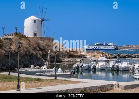 Parikia, Paros, GR - 22. August 2025: Eine traditionelle Windmühle steht in der Nähe des Hafens mit einer Fähre in der Ferne Stockfoto