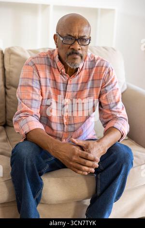 Ranghoher afroamerikaner mit Brille, der auf einem beigen Sofa im Wohnzimmer liegend sitzt Stockfoto