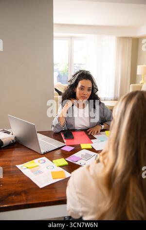 Weibliche Kollegen, die im Wohnzimmer mit Laptop, Diagrammen und Haftnotizen zusammenarbeiten Stockfoto