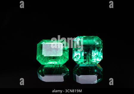 Zwei grüne Edelsteine werden auf schwarzem Hintergrund angezeigt. Die Steine werden in die Form eines Smaragds geschnitten und von einer Lichtquelle beleuchtet Stockfoto