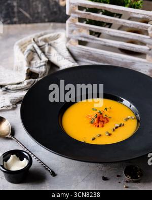Genießen Sie eine lebhafte Kürbissuppe, die wunderschön mit frischen Kräutern und Gewürzen garniert wird Stockfoto
